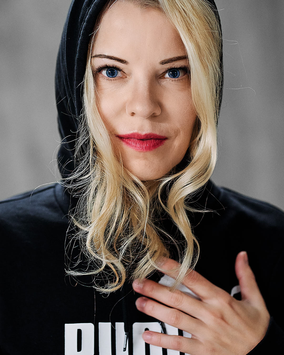 woman looking straight into camera. blue eyes and red lips. she is wearing a black hoody