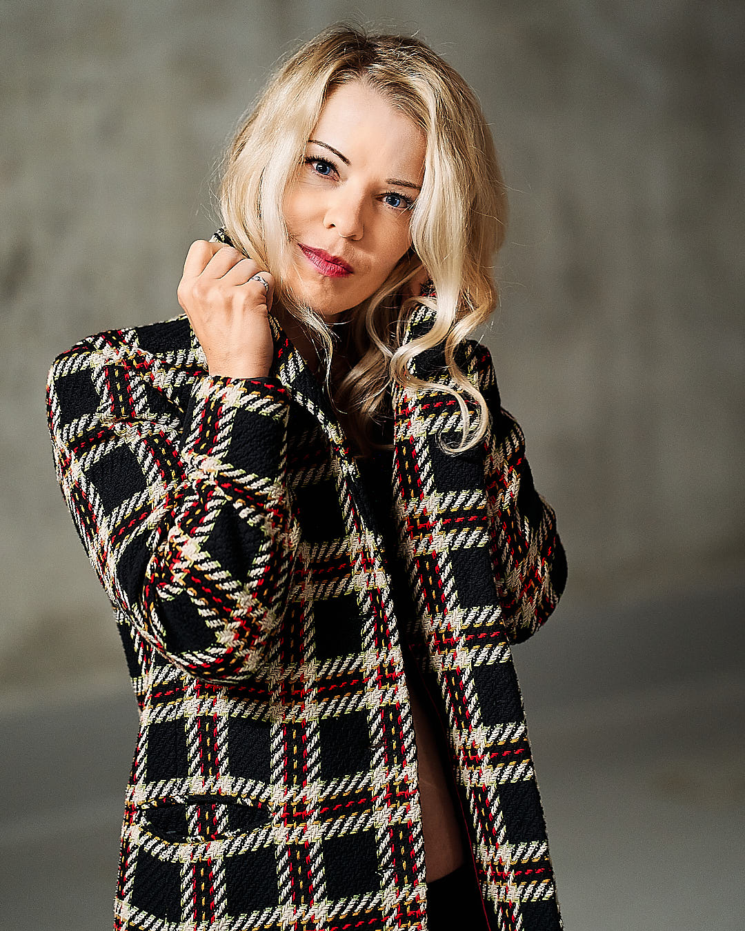 woman looking straight into camera while having her hands raised to her collar. she is blond with blue eyes